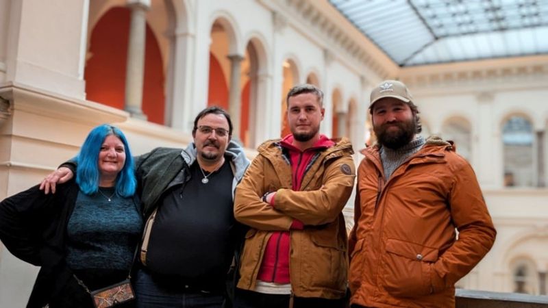 Four friends smiling together in a grand arcaded hall with a glass roof